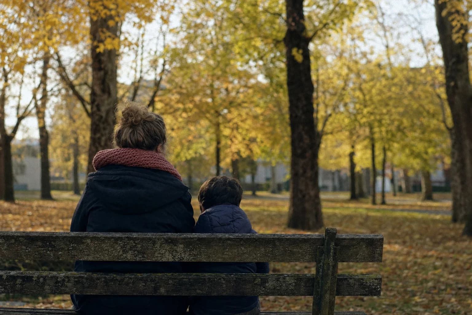 Un parent et son enfant assis sur un banc, dans un parc en automne