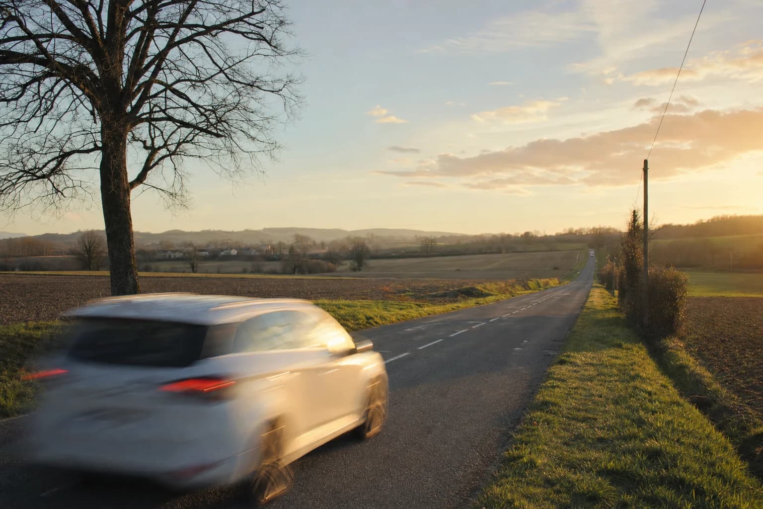 Une voiture file sur une route droite à travers les champs, au coucher du soleil