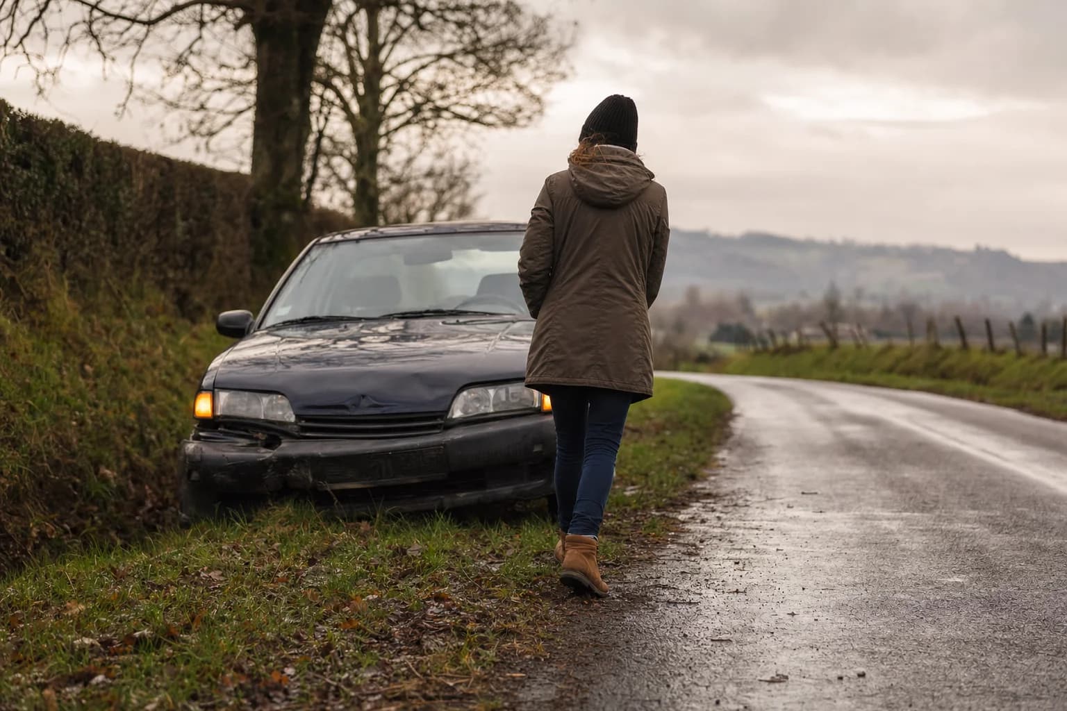 Une voiture au pare-chocs enfoncé, arrêtée au bord d’une route de campagne après la pluie