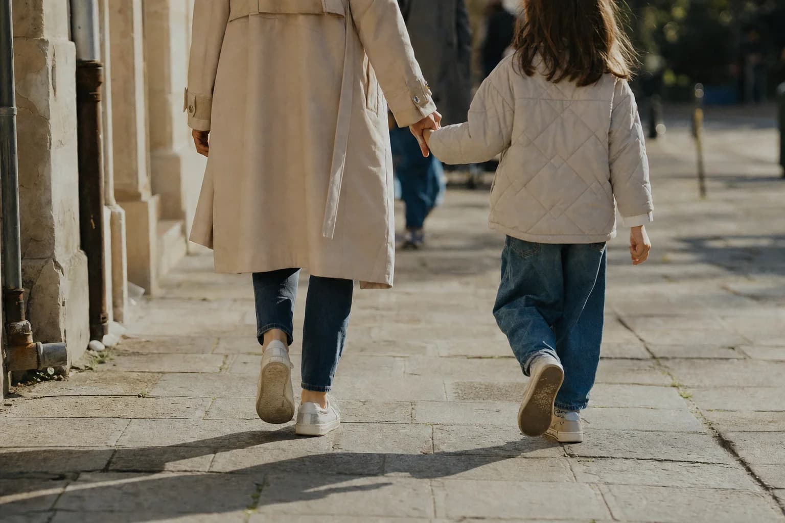 Un parent et son enfant marchent main dans la main sur un trottoir ensoleillé