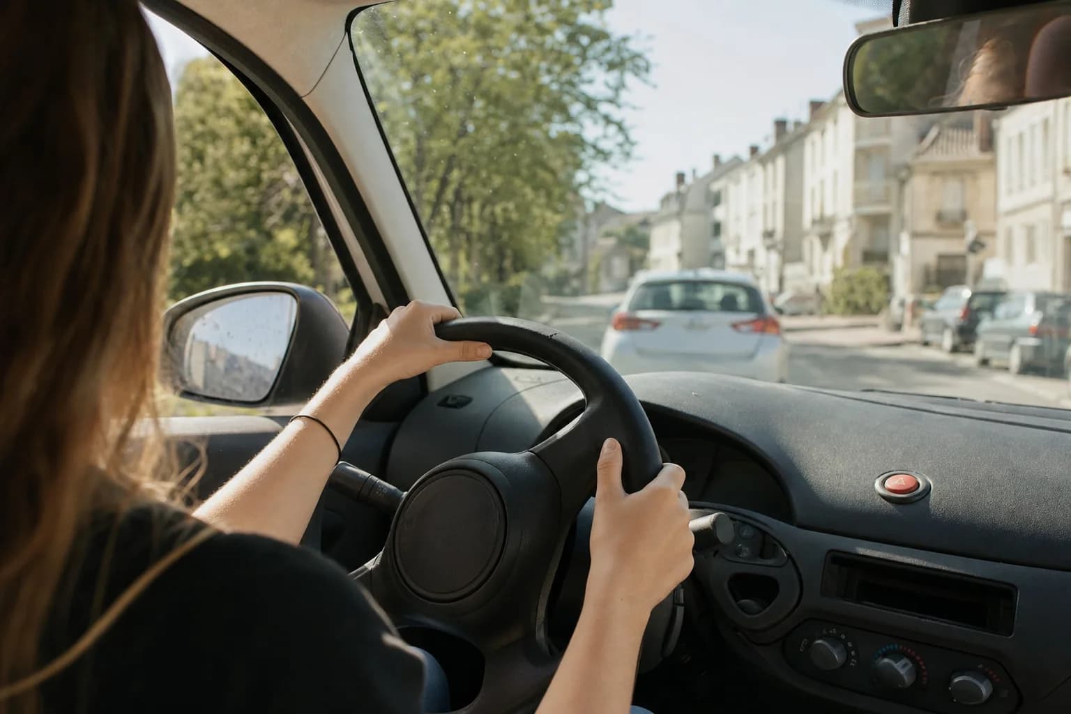 Une jeune conductrice, les mains sur le volant, dans une rue ensoleillée