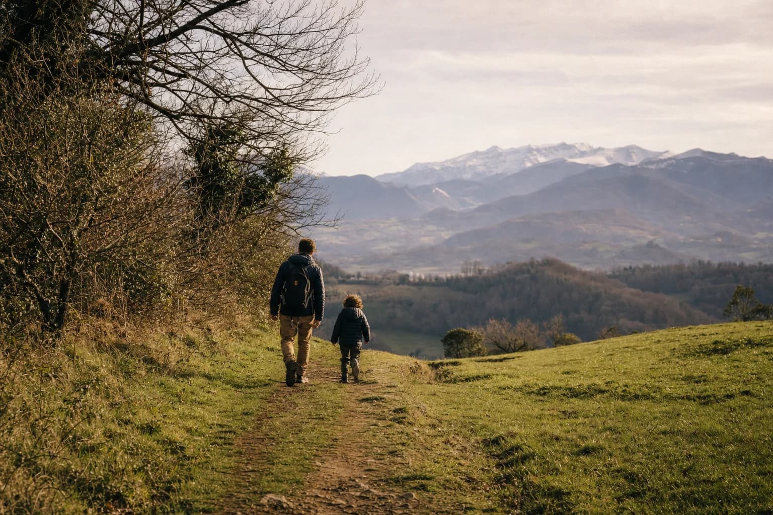 Un père et son jeune enfant marchent sur un chemin de colline, face aux montagnes