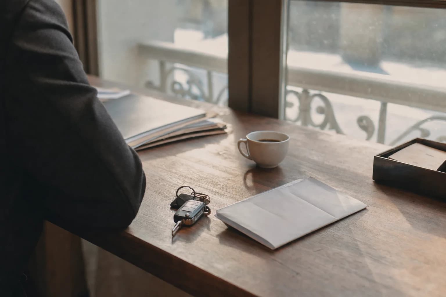 Des clés de voiture et une enveloppe sur un bureau en bois, près d’une tasse de café
